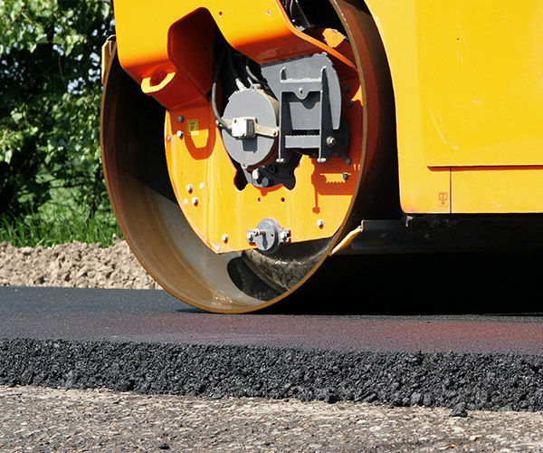 close-up, Road construction works with roller compactor machine and asphalt finisher. Road roller laying fresh asphalt pavement on top of the gravel base during road construction. High quality photo
