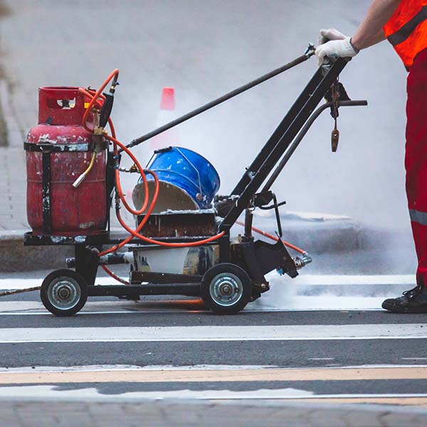 Process of making new road surface markings with a line striping machine, workers improve city infrastructure, demarcation marking of pedestrian crossing with a hot melted paint on asphalt pavement