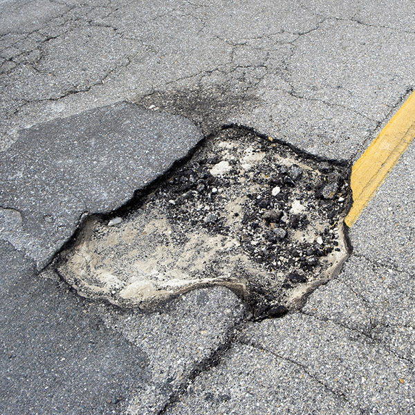 Damaged american road surface with deep pothole. Ruined street in urgent need of repair.