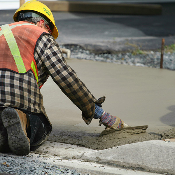 Construction worker uses a hand trowel to smooth out concrete on a new sidewalk project.