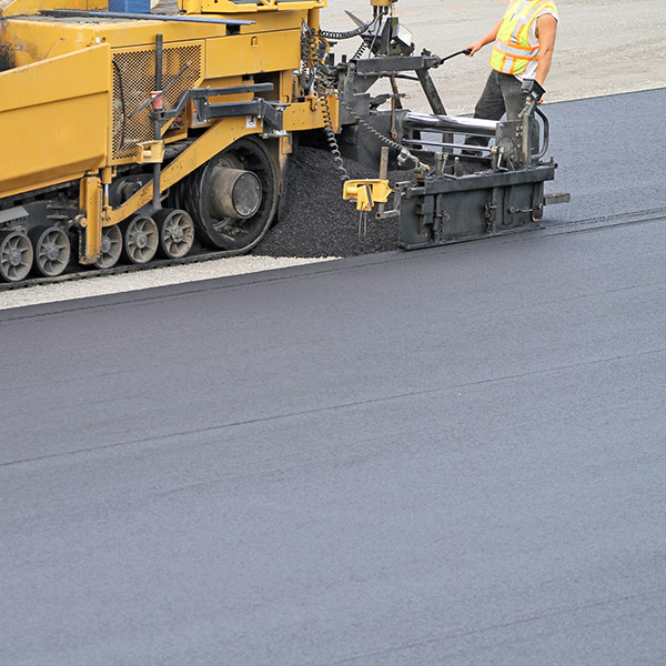 Side view of an asphalt paving machine at work paving a large parking lot, shot shallow dof and copy space.